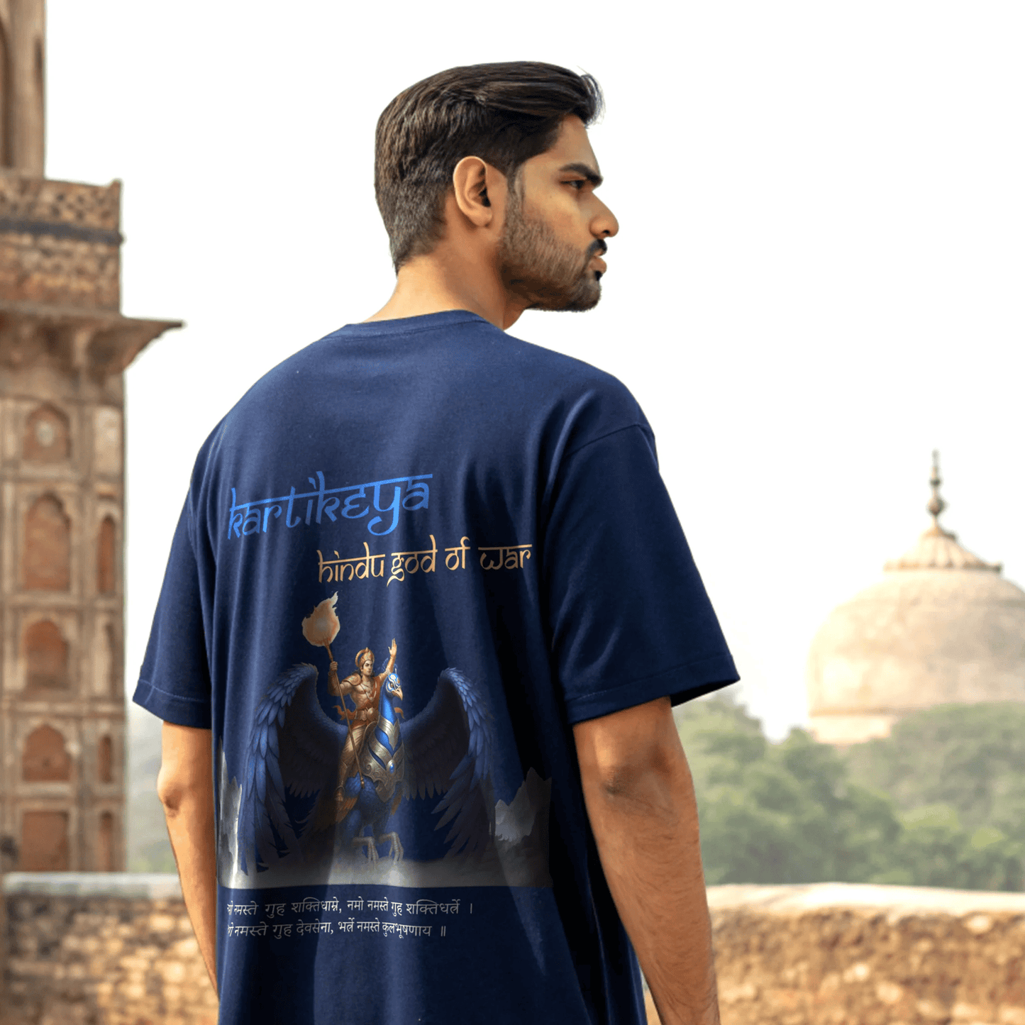 Man wearing a royal blue t-shirt with a graphic design and text, standing in front of a historical building By OFF THE RACK