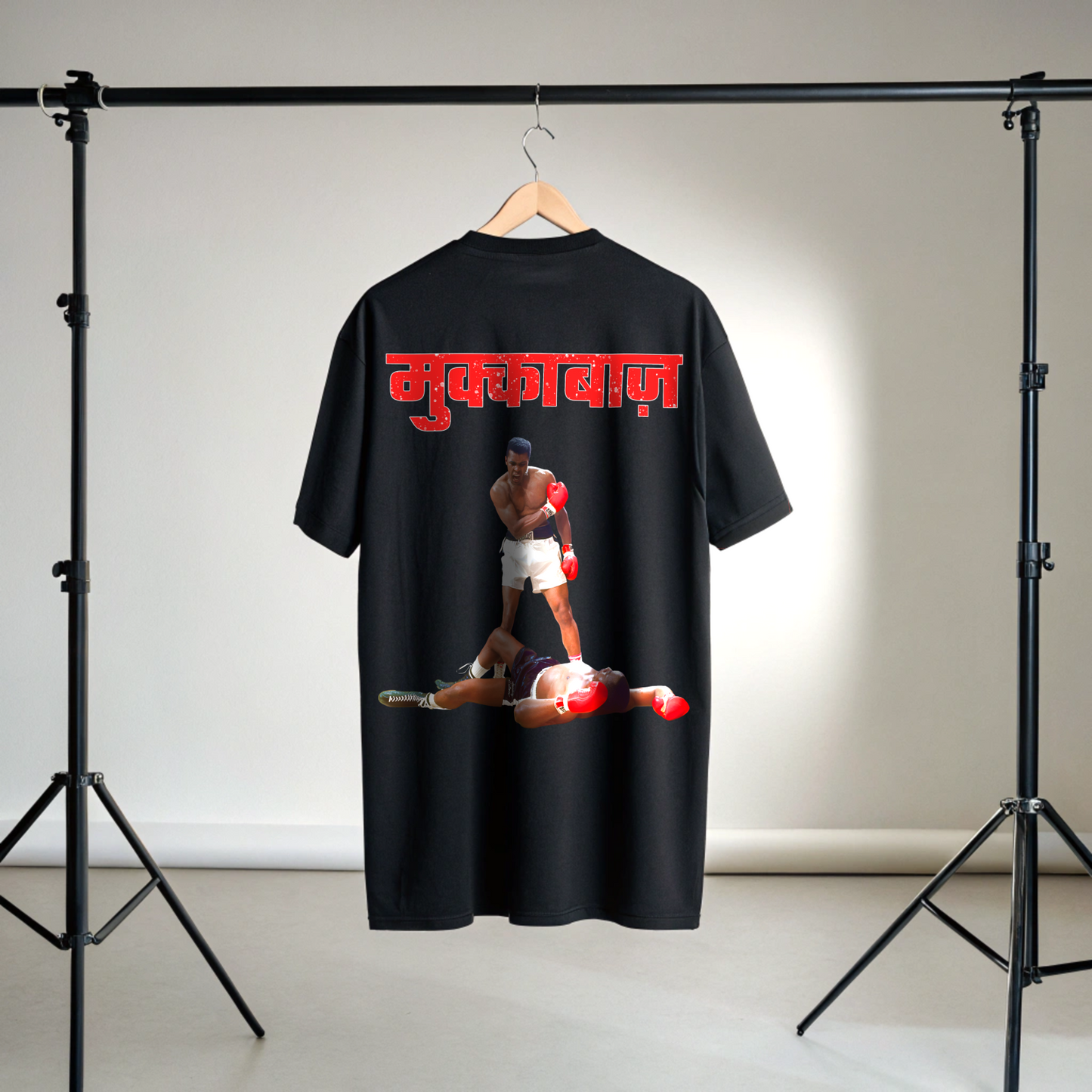 Black t-shirt with a graphic of Two boxer and Red MUKKEBAAZ text on a hanger against a neutral background in studio setup By OFF THE RACK