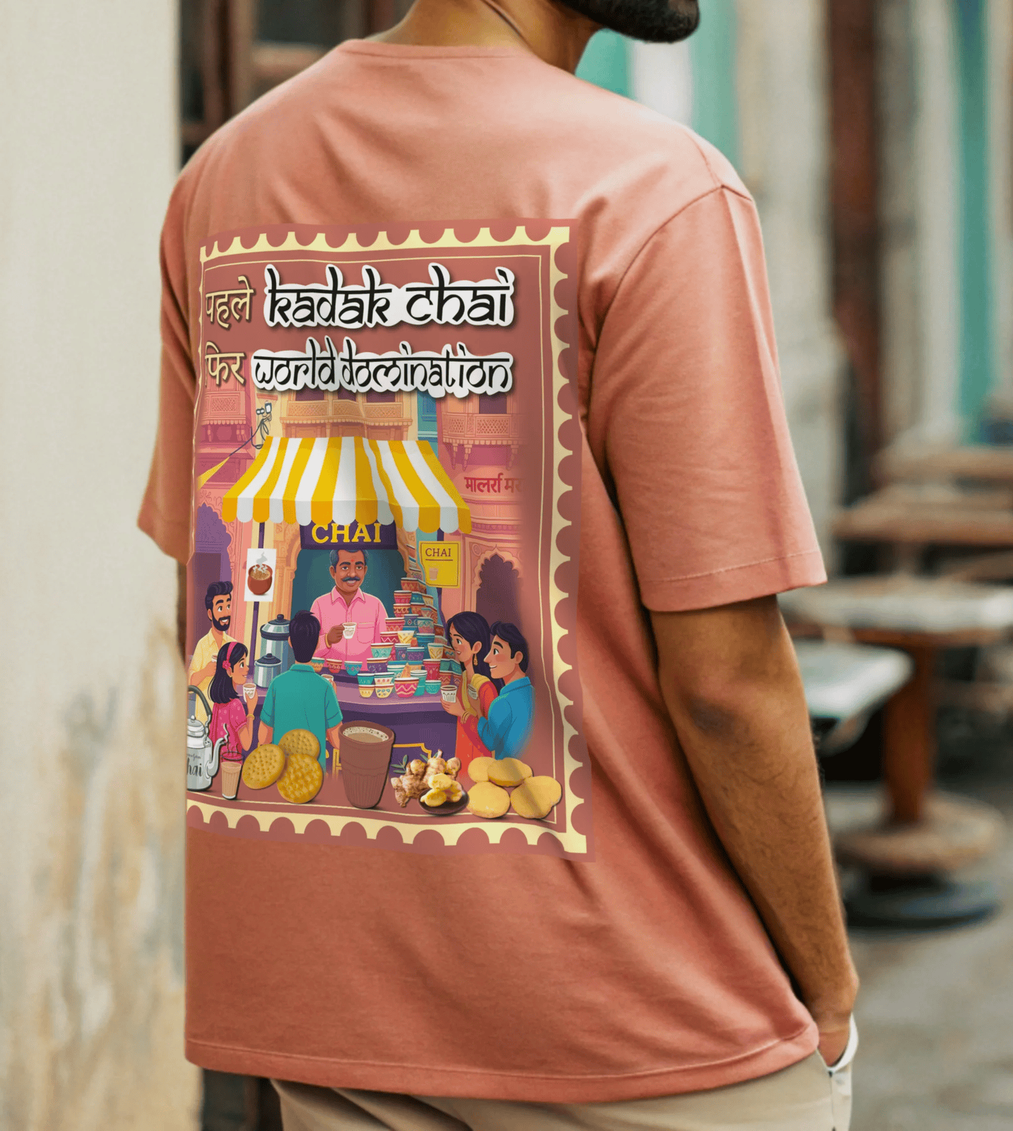 Person wearing coral t-shirt with a colorful graphic on the back, featuring people around a chai stall standing near a chai stalll By OFF THE RACK