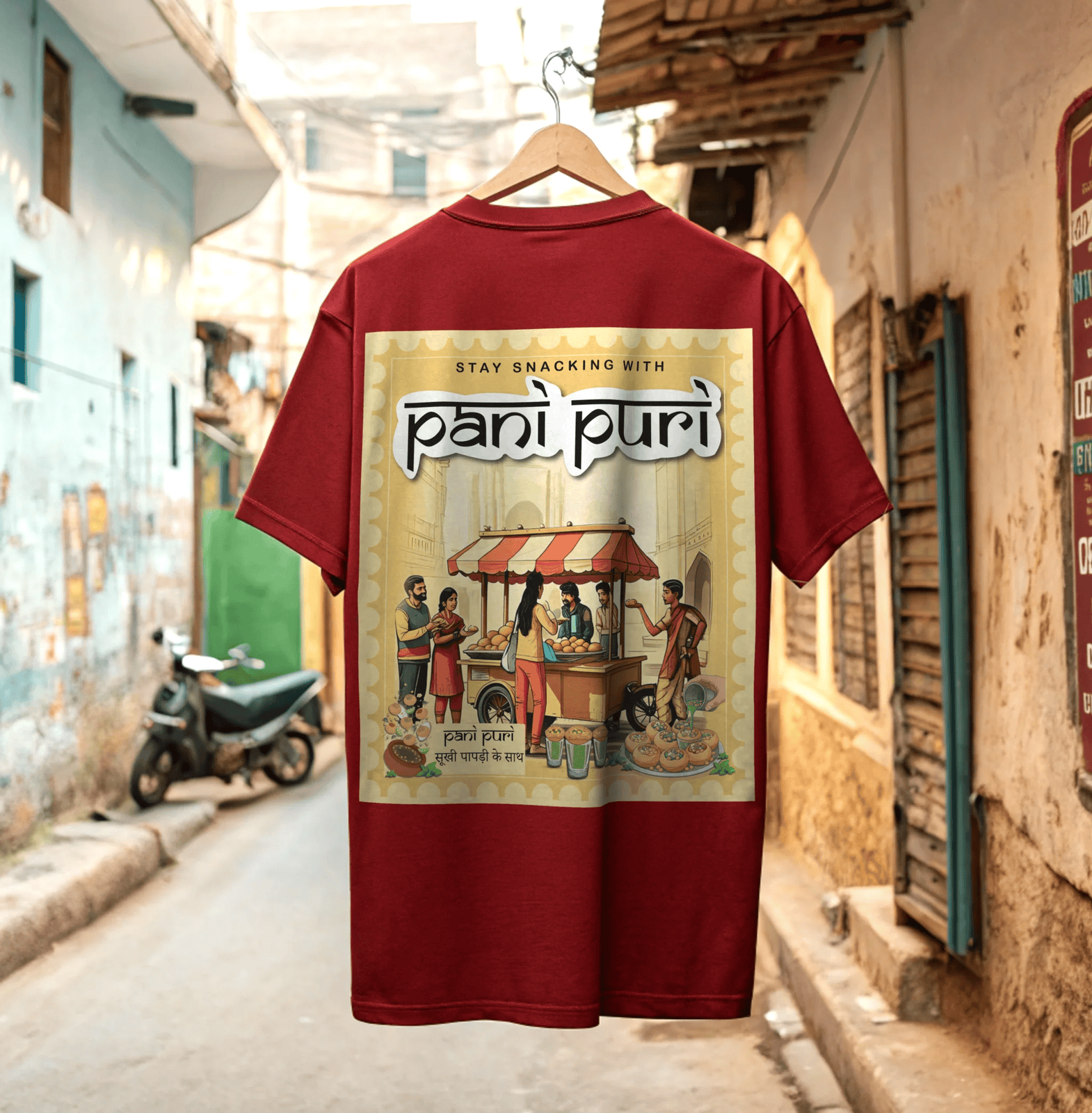 Red t-shirt with 'pani puri' graphic design on a hanger against a desi street background By OFF THE RACK